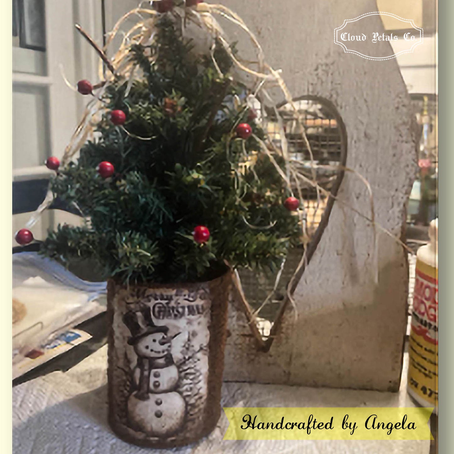 Small Christmas tree in a decorated vase with a snowman design, placed on a surface.