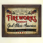 A vintage style 4th of July fireworks sign with the text 'Old Glory 1776 FIREWORKS COMPANY God Bless America' and American flags, sparkles, and fountains mentioned below. The sign is presented in a wooden frame.