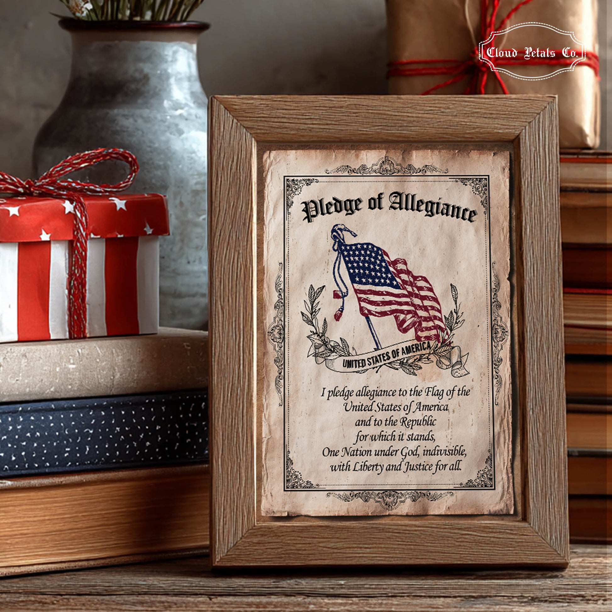 Framed Pledge of Allegiance with American flag design on a wooden surface with gift and books in the background.